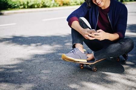 Cropped image of young man sitting on skateboard and textingの写真素材