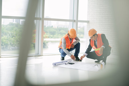 Civil engineers discussing blueprint on the floorの写真素材