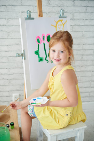 Smiling girl sitting in front of easel with canvas