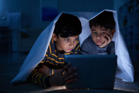 Indian children watching movies on tablet at nightの写真素材