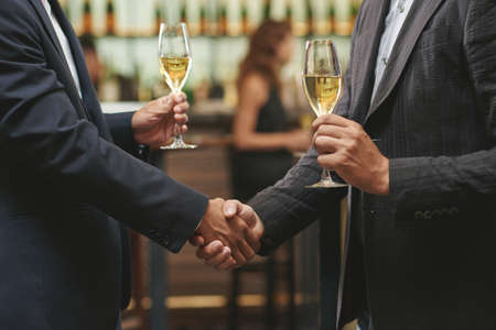 Hands of men shaking hands and drinking white wineの写真素材