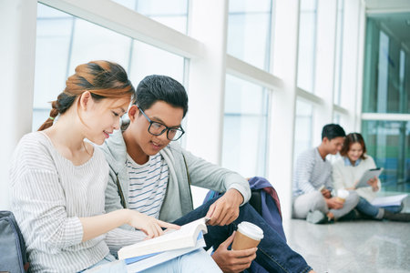 Smiling university students reading book before class