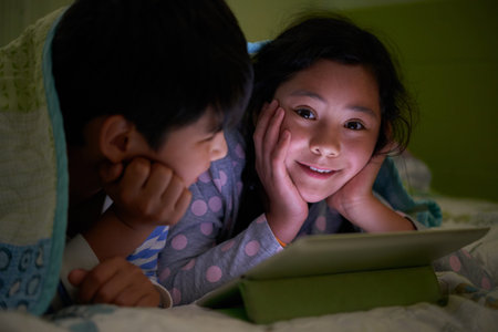 Smiling girl enjoying watching cartoons with her brotherの写真素材