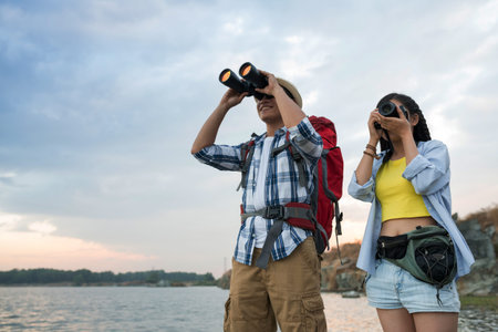 Young tourists looking at binoculars ant taking photos by lakeの写真素材