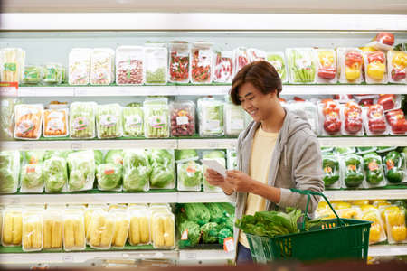 Young man reading grocery list when shopping in supermarketの写真素材