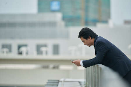 Vietnamese entrepreneur standing on rooftop and reading text messageの写真素材