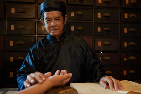 Asian senior man checking pulse of patient to diagnose illnessの写真素材