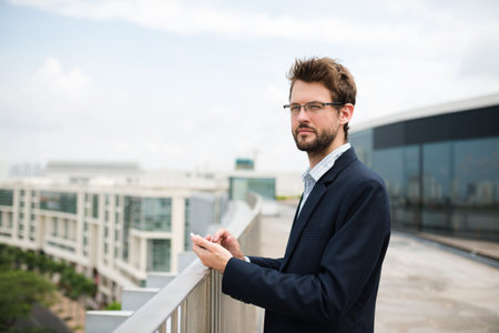 Young businessman with smartphone standing on top of the building