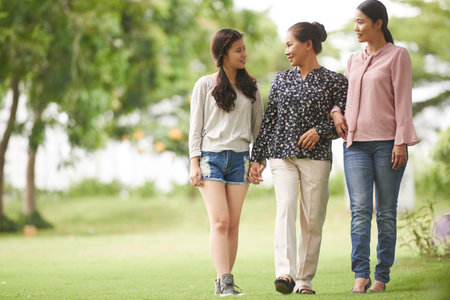 Cheerful Vietnamese teenage girl with her mother and grandmother walking in park