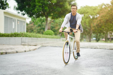 Vietnamese man in glasses riding bicycle on rainy dayの写真素材