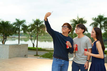Happy Asian teens having refreshing drinks and taking photo togetherの写真素材