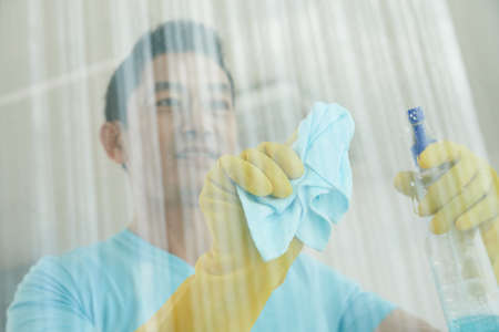 Smiling mature Asian man in gloves cleaning windowの写真素材