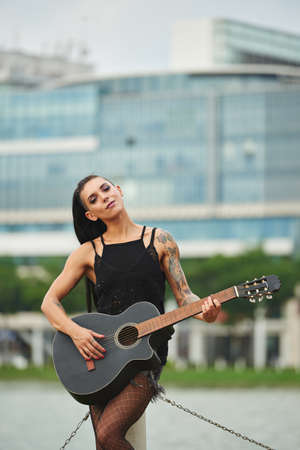 Portrait of alternative smiling girl with many tattoos playing guitarの写真素材