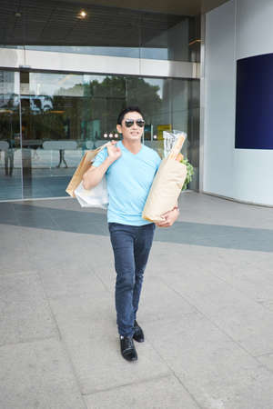 Happy Asian man with shopping bags leaving supermarketの写真素材