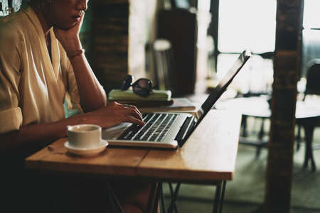 Close-up image of tired business lady reading data on laptop and drinking coffeeの写真素材