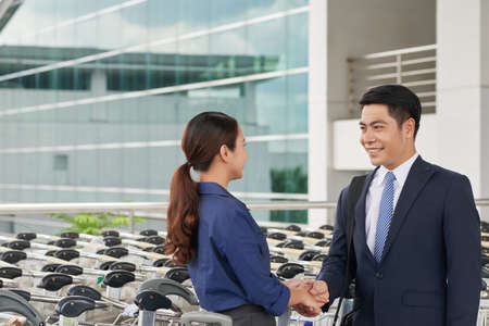 Portrait of modern Asian business partners, man and woman, shaking hands and smiling greeting each otherの写真素材