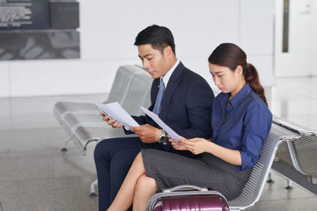 Portrait of two modern Asian  business people, man and woman, waiting for departure on business trip  in waiting zone of airport with big suitcasesの写真素材