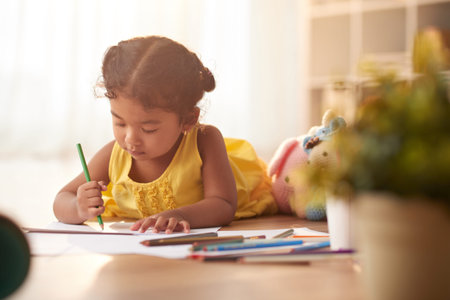 Mixed race little girl lying on floor and drawing picture with colored pencil, portrait shot