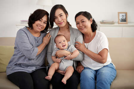 Portrait of three generations of woman in Asian family, posing on sofa at home smiling happily looking at camera Women in Asian Familyの写真素材