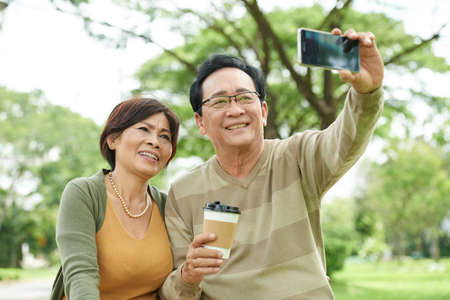 Joyful Vietnamese senior couple taking selfie in parkの写真素材