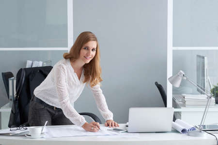 Pretty project manager making corrections in blueprint of the buildingの写真素材