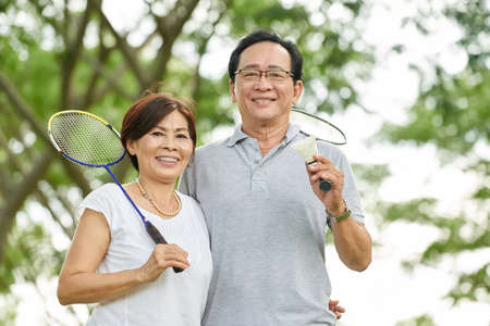 Portrait of sporty aged Asian couple with badminton racketsの写真素材