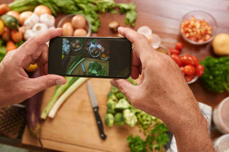 Man preparing meal and taking picture with smartphone of the ingredientsの写真素材