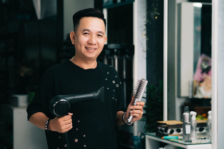 Portrait of Vietnamese smiling hairdresser with hairbrush and fan in his handsの写真素材
