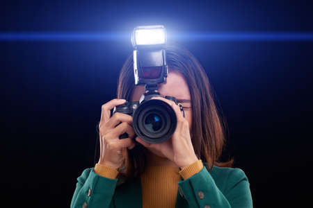 Female photographer taking photos with flash, isolated on darkの写真素材