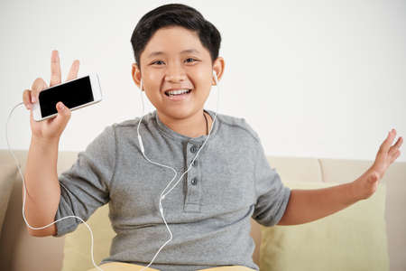 Cheerful Vietnamese boy enjoying music in his smartphoneの写真素材