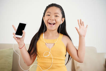 Portrait of happy excited Vietnamese girl listening to music in smartphone applicationの写真素材