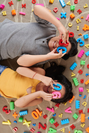 Children lying on the floor and covering their eyes with plastic figures, view from the top
