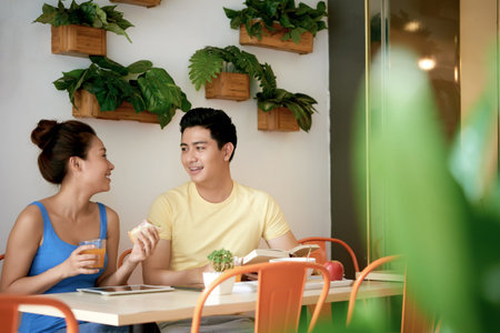 Young Vietnamese couple eating breakfast and chatting in kitchen