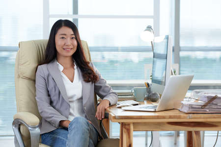 Pretty female head of the company sitting on chair in officeの写真素材