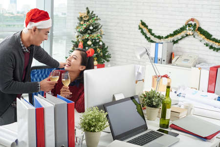 Two happy office workers celebrating New Year with champagne at workplaceの写真素材