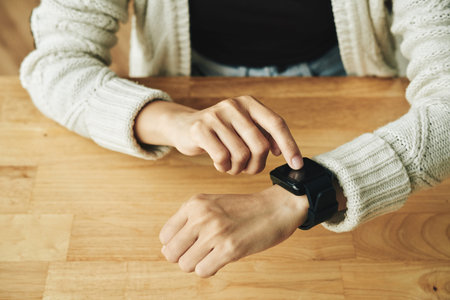 Close-up shot of unrecognizable woman wearing knitted cardigan using smartwatch while sitting at...