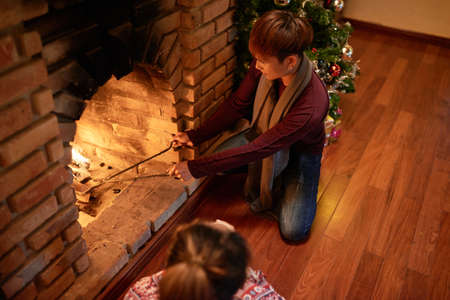 Man using tongs to check firewood in chimney on Christmas nightの写真素材