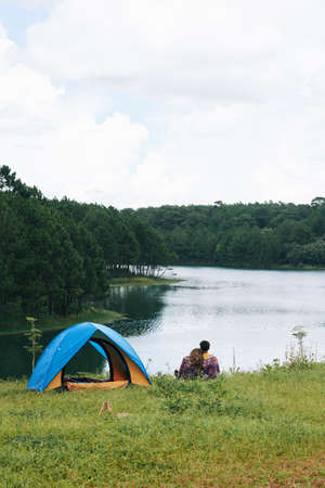 Young couple camping by lake, view from the backの写真素材