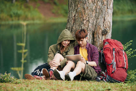 Vietnamese young travelers sitting under rives and reading something on tablet computerの写真素材