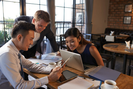 Cheerful Vietnamese businessman showing document on tablet computer to his colleagues