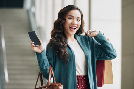 Excited young woman with shopping bags and smartphoneの写真素材