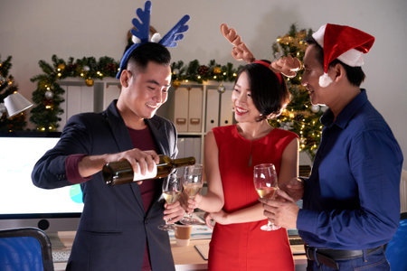 Cheerful businessman pouring wine into glasses of colleaguesの写真素材
