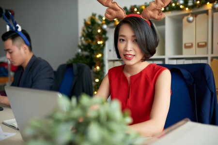 Pretty Vietnamese business lady with deer horns on her head working in office