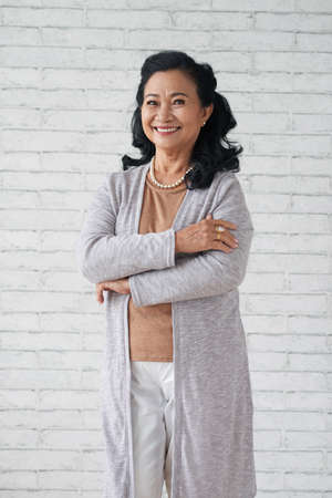 Portrait of cheerful Vietnamese senior woman standing at the wallの写真素材