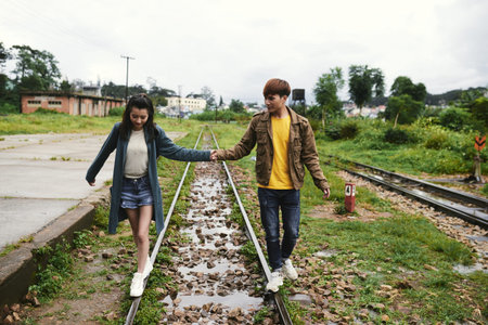 Asian young couple holding hands and walking along railwayの写真素材