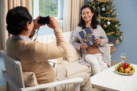 Senior man taking photo of his wife near Christmas treeの写真素材