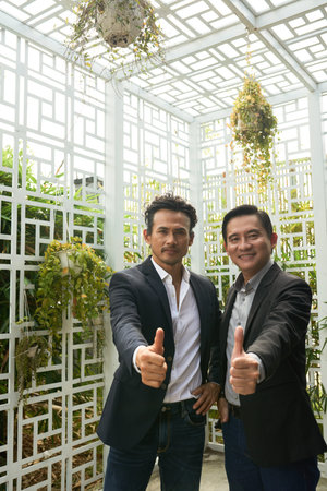 Happy mature Vietnamese business people showing thumbs-up