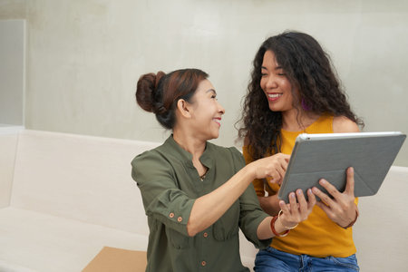 Happy adult woman and her mother using application on digital tablet