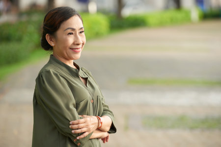 Happy pensive aged Vietnamese woman standing outdoorsの写真素材