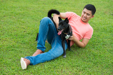 Asian young man playing with his dog on green meadowの写真素材